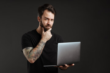 Bearded brunette man with tattoo think and using laptop