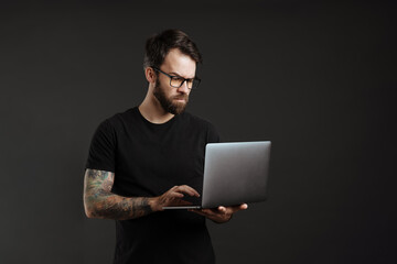 Bearded brunette man in eyeglasses think and using laptop