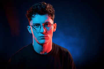 Against black background. Neon lighting. Young european man is in the dark studio