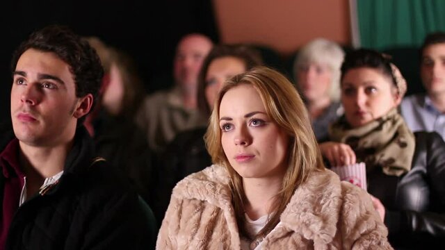 Caucasian Couple sat in Cinema Theatre watching a film or movie whilst eating popcorn. Tracking Shot. Stock Video Clip Footage