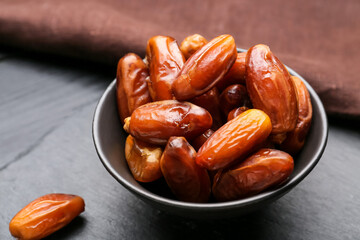 Bowl with sweet dried dates on dark wooden background, closeup
