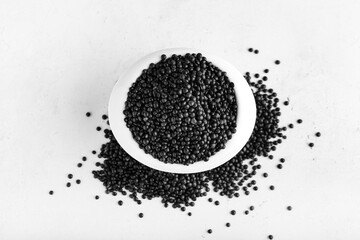 Bowl with black lentils on light background