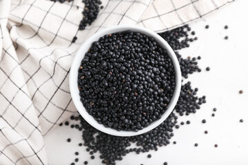 Bowl with black lentils on light background