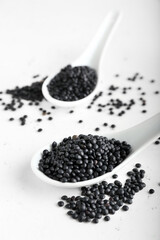 Spoons with black lentils on light background
