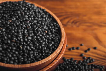 Fototapeta na wymiar Bowl with black lentils on wooden background