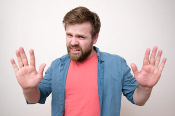 Disgruntled bearded man makes a stop gesture with his palm, a gesture of protection and looks disgustedly. White background.