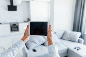 Digital tablet in hands. Young woman is indoors in smart house room at daytime