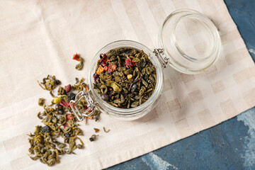 Jar of dry green tea on color background
