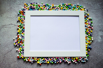 White frame with multicolored small balls around. Against the background of cracked concrete. Copy space