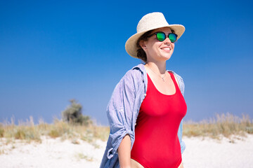 Beautiful young woman smiling relaxing on summer beach, sunbathing wearing red bikini, straw hat, sunglasses.Enjoying life in paradise, long awaited vacation.Advertising for travel company and agency