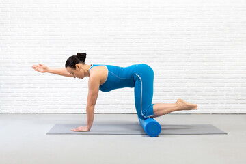 Fototapeta premium Adult caucasian woman practice pilates with props in fitness studio indoor, bird dog drill with one raised arm and foam roller under her knees, selective focus.