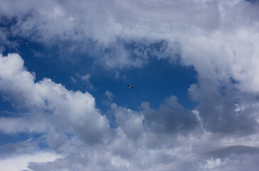 Blue sky with a group of clouds, among which an airplane flies 