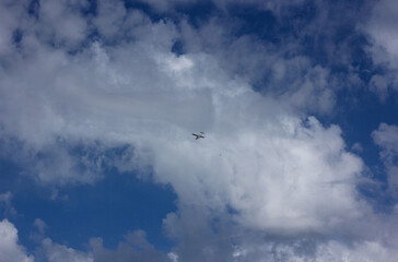 Blue sky with a group of clouds, among which an airplane flies 