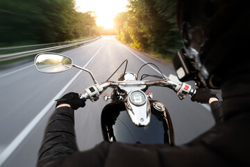 The motorcyclist is riding through the empty asphalt road in the evening - obrazy, fototapety, plakaty