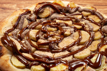 Banana pizza with chocolate sauce and cinnamon powder, served on a wooden table. View from the top.