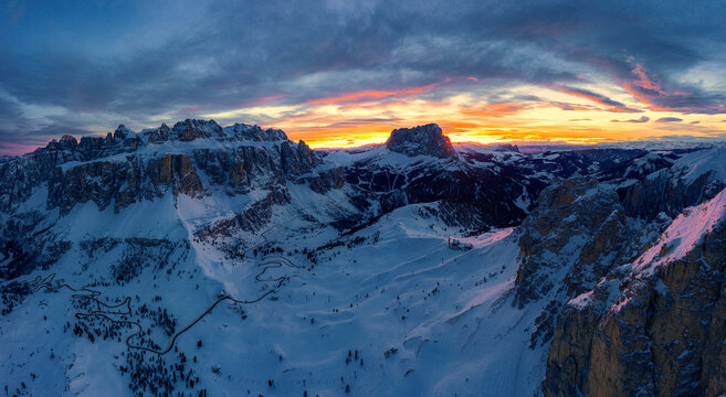 Clouds in the burning sky at sunset over Sassolungo and Sella Group mountains covered with snow, Dolomites, South Tyrol, Italy