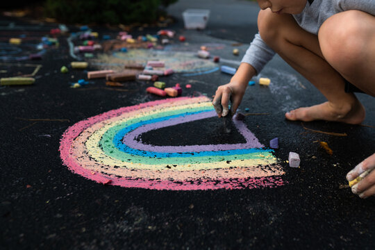 low angle view of young boy drawing rainbow art with chalk on pavement