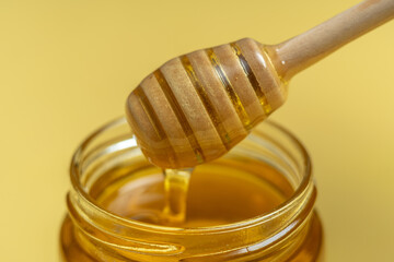 Natural healthy bee honey in a jar and on a wooden stick. Closeup and yellow background