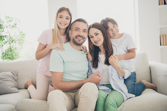 Photo of optimistic cute full family with two kids hug sit on sofa wear t-shirts trousers at home