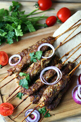 Appetizing lula kebab on wooden sticks with onion rings and herbs. Lula kebab preparation. Ramadan.