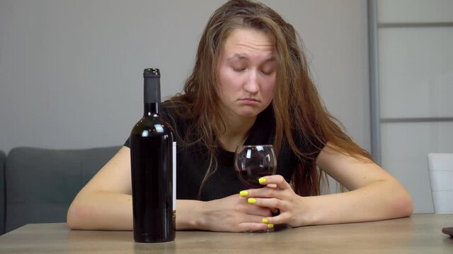 woman sad and devastated alcoholic sits at home on couch couch drinking red wine holding glass completely drunk looks depressed lonely and suffers from hangover from alcoholism and alcohol abuse
