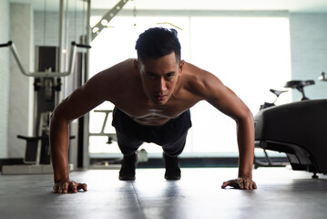 Muscular bodybuilder guy doing push ups in gym.