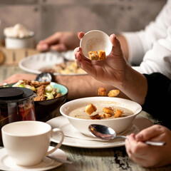 Woman adding croutons to bowl of mushroom cream soup on table. Close up shot. Nutritious wholesome food. Vegetarian diet meal. Delicious and healthy lunch or dinner.