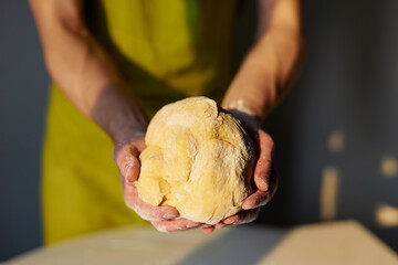 Homemade biscuits baking, Easter pastry preparing or tasty cookie concept. Male chef in green apron holds in hands a ball of dough made for bread, pizza or pastry. High quality photo