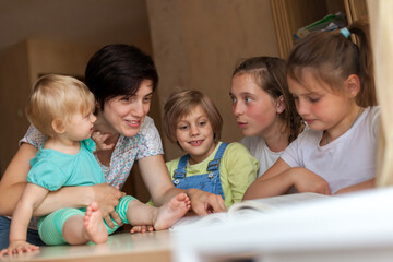 Woman with four children at   table reading   book