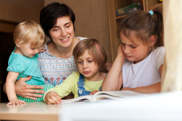 Fototapeta na wymiar Woman with three children at table reading book