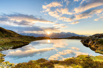 The sun and clouds reflected in the Arcoglio Lake at sunrise, Valmalenco, Valtellina, Lombardy, Italy
