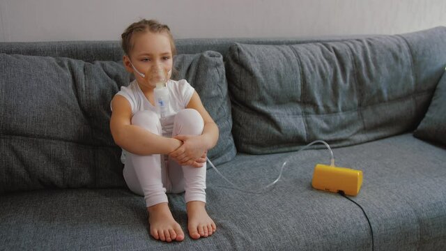 Little girl makes inhalation with medical nebulizer while sitting on bed