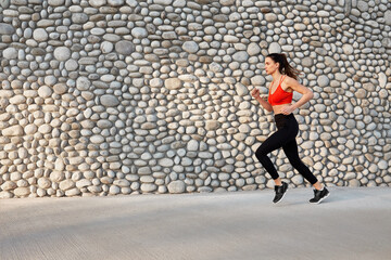 Sports woman running past grey stone wall
