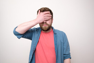 Man in stress or he has a headache, he covered eyes with hand, standing on a white background. Psychological concept.