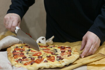Woman cuts homemade pizza with tomatoes and champignes on the table
