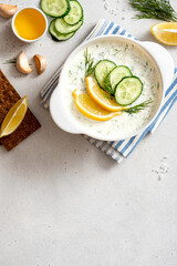 Tzatziki - traditional Greek sauce. Sauce made from yogurt, cucumber, garlic, herbs, lemon, and olive oil. Homemade tzatziki in a white bowl on a gray concrete background top view. Free space for text
