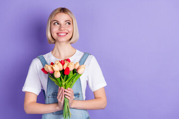 Photo of nice optimistic short hairdo blond lady hold flowers look empty space wear white t-shirt isolated on violet background