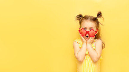 Little child girl in striped swimsuit and red funny summer sunglasses surprised expression looks at camera posing on yellow background, studio portrait.Advertising of children's products and sale
