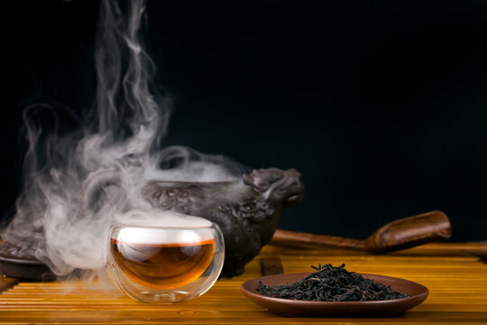 Chinese tea ceremony. Clay teapot with red tea Lapsang souchong on a black background, heap of tea and glass thermo cup of hot tea with vapour.