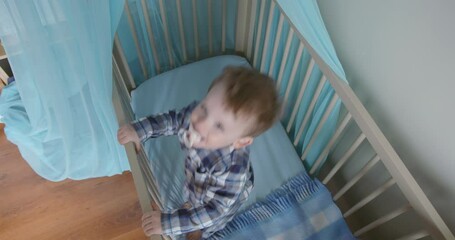 Baby boy having fun jumping up and down in his crib, topview slow motion