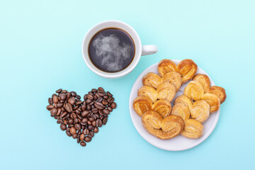 Steaming coffee cup, heart shaped cookies, heart shaped coffee beans on a blue background, top view. Morning breakfast. Breakfast for loved ones.