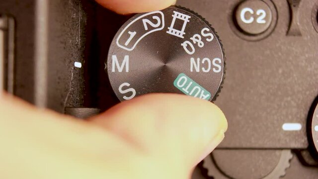 Extreme macro close up of a hand adjusting Digital Camera Mode Dial Settings from Manual mode setting to Auto mode. Selective focus of mode dial