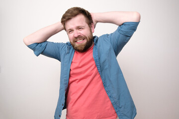 Shy, uncertain man smiles modestly with hands behind head. White background.