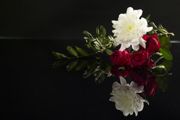 Beautiful bouquet of flowers: red roses, white chrysanthemums, green leaves on black background