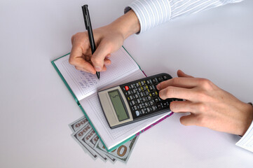  Men's hands with a pen, notepad, calculator and money on a white background. Home finance. Financial accounting. Close-up