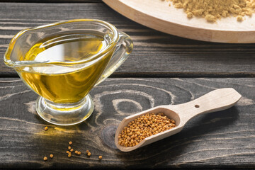 Mustard seeds in the spoon and mustard oil on brown wooden table
