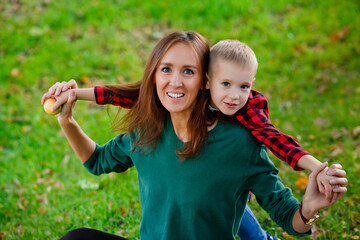 A large portrait of a young mother and son in a park on a green background. happy family: a mother and a boy play, hugging, on an autumn walk in nature.