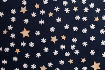 Small white snowflakes and wooden stars on a dark acrylic background taken close up
