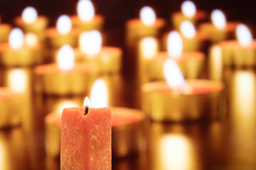 closeup of burning red candle among many others in church or Buddhist temple