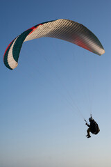 Paraglider flying over a cliff with blue sky, during the golden hour in Majorca.